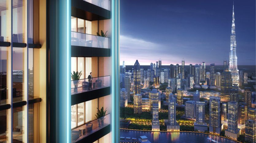 View from the balcony of a high-rise apartment in Dubai at night, overlooking a bustling cityscape with illuminated skyscrapers and a prominent tower in the distance.