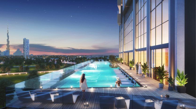 A luxurious rooftop pool at dusk, with a woman standing at the edge. The Dubai city skyline sparkles in the background under a starry sky. Elegant seating and plants enhance the serene atmosphere.