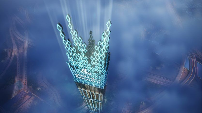 Aerial view of a futuristic skyscraper in Dubai illuminated by blue lights, projecting beams of light into a hazy sky, surrounded by roads and clouds.