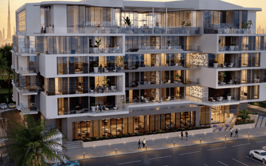 Un bâtiment moderne de plusieurs étages dans les jardins d'Ayana, doté de grandes fenêtres en verre et de balcons, est éclairé par un éclairage chaleureux pendant la soirée. Les gens marchent sur le trottoir et les voitures sont garées dans la rue. Les toits de la ville sont visibles en arrière-plan et des palmiers bordent la zone.