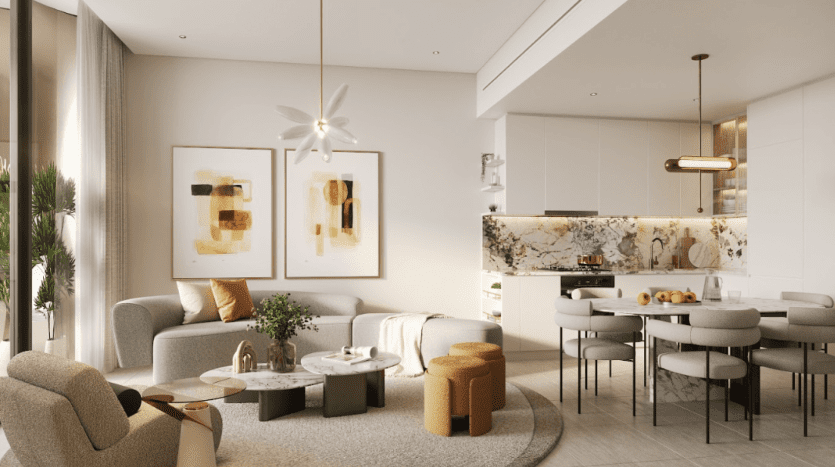 Un salon et un coin cuisine modernes et ouverts dans One Residences avec des murs et un sol aux tons clairs. Le salon comprend un canapé gris, des tables basses rondes et des œuvres d'art abstraites. La cuisine a un dosseret en marbre, des armoires blanches et une table à manger avec des chaises grises.