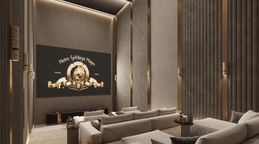 Un luxueux home cinéma dans les résidences Fairmont est doté de canapés blancs moelleux contre des murs beiges aux panneaux verticaux. Le grand écran affiche fièrement le logo MGM, tandis qu'un éclairage doux baigne l'espace dans une ambiance chaleureuse et élégante, incarnant un style de vie raffiné.