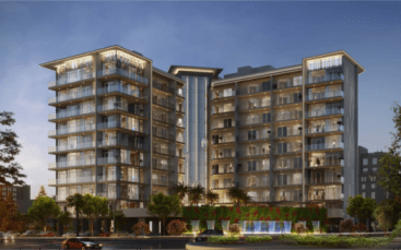 Au crépuscule, l'immeuble d'appartements Floarea Grande se présente moderne et illuminé. La structure dispose de nombreux balcons et de grandes fenêtres, avec une entrée paysagée avec des palmiers et une fontaine à eau au rez-de-chaussée.