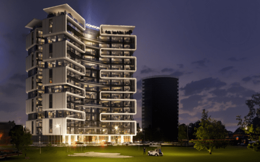Un bâtiment moderne à plusieurs étages avec des sections éclairées se dresse au crépuscule sur un ciel qui s'assombrit, rappelant la beauté sereine d'un terrain de golf. Les balcons aux formes uniques ajoutent à son charme, tandis qu'au premier plan, une petite voiturette de golf est garée sur une zone herbeuse avec des arbres à proximité.