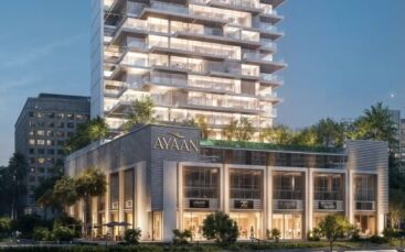 Ayaan Heights 1 by IGO est un immeuble moderne de plusieurs étages baptisé "Ayaan", qui propose des magasins aux étages inférieurs et une tour au-dessus avec des balcons et de la verdure, magnifiquement illuminée le soir.