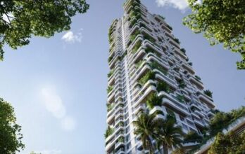 Un grand gratte-ciel moderne, Talea by Beyond, avec des balcons blancs ornés de plantes et d'arbres verdoyants, vus d'en bas sur fond de ciel bleu et encadrés par des branches feuillues.