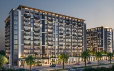 Immeubles modernes à plusieurs étages avec de grandes fenêtres et des balcons, illuminés au crépuscule. Des palmiers bordent la rue devant Windsor House de Ellington Properties, avec des voitures garées à proximité, créant une atmosphère urbaine haut de gamme.