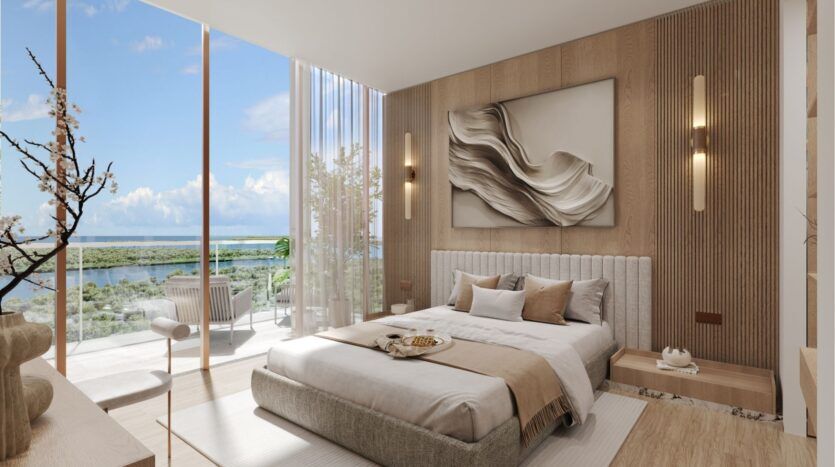 Chambre moderne à wynwood horizon de Imtiaz avec des tons neutres, un grand lit, de l'art mural abstrait, des fenêtres allant du sol au plafond et un balcon offrant des sièges extérieurs et une vue pittoresque sur l'eau et la verdure sous un ciel radieux.