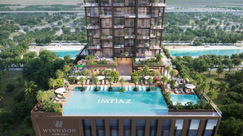 Vue aérienne de la tour moderne Wynwood Horizon de Imtiaz, qui comprend une piscine sur le toit, des espaces de détente, une végétation luxuriante et des balcons. Des palmiers entourent le bâtiment, avec un grand parc et des routes en arrière-plan. La piscine porte l'inscription "IMTIAZ".