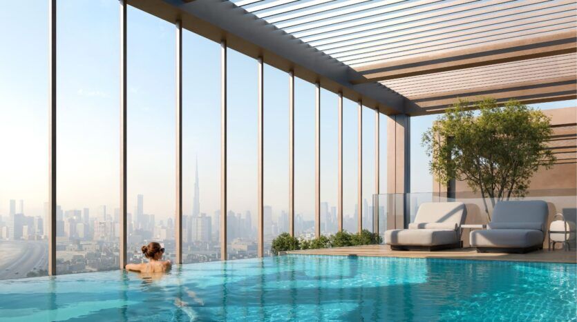 Une personne nage dans la piscine à débordement de Wynwood Horizon de Imtiaz, profitant des chaises longues sur le toit, des arbres et de l'horizon dégagé de la ville sous une pergola moderne.