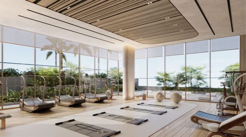 Salle de sport moderne avec de grandes fenêtres à Wynwood Horizon de Imtiaz, laissant entrer la lumière naturelle et comprenant des tapis de yoga, des ballons d'exercice et des équipements cardio. Les plantes tropicales et les palmiers à l'extérieur créent une atmosphère ouverte, aérée et relaxante.