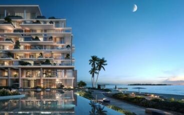 Un bâtiment moderne en bord de mer à Silena Dubai Islands dispose de balcons en verre donnant sur une piscine calme, des palmiers et une plage de sable au crépuscule, sous un croissant de lune. Le ciel passe du bleu profond au pâle le long de l'horizon.