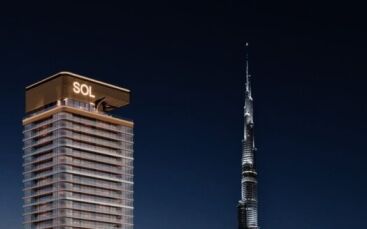 Une tour moderne, la Sol Luxe Tower, est illuminée la nuit et se dresse à côté de la Burj Khalifa, plus haute et semblable à une aiguille, dans un ciel sombre.
