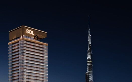 Une tour moderne, la Sol Luxe Tower, est illuminée la nuit et se dresse à côté de la Burj Khalifa, plus haute et semblable à une aiguille, dans un ciel sombre.