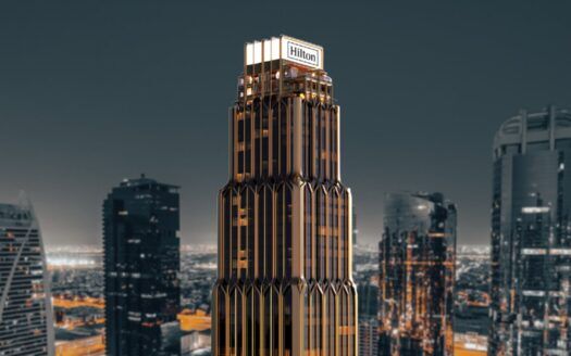 Grand gratte-ciel moderne surmonté de l'enseigne "Hilton", les résidences Hilton se détachent sur un paysage urbain de gratte-ciel à la tombée de la nuit, avec des accents dorés et sombres saisissants.