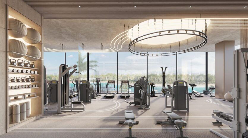 Salle de sport moderne au Caden avec de grandes fenêtres, diverses machines d'exercice, des poids libres et des bancs. La lumière naturelle remplit la pièce spacieuse qui donne sur les palmiers et l'eau. Les plafonniers circulaires ajoutent du style.