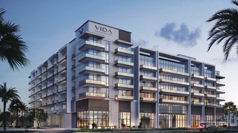 Immeuble moderne de plusieurs étages avec balcons en verre et grandes fenêtres, portant l'inscription "VIDA RESIDENCES" au sommet. Des palmiers et des aménagements paysagers encadrent la scène, dans un ciel crépusculaire - une vue emblématique de Vida Residences Saadiyat Island.