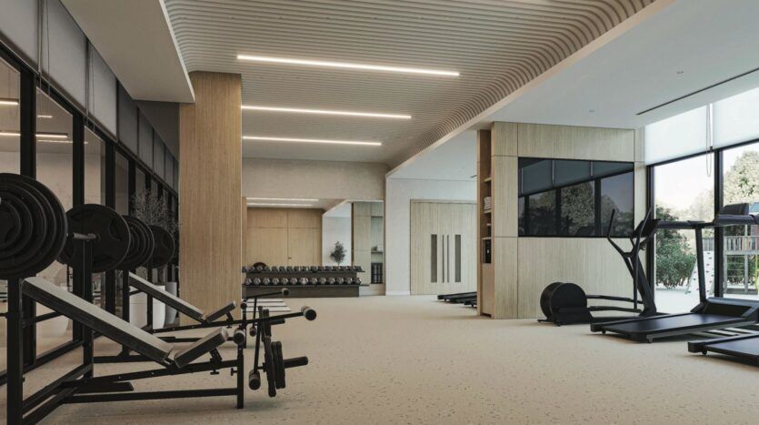 Salle de sport spacieuse et moderne à Vida Residences Saadiyat Island avec des bancs de musculation, des haltères, des tapis de course, de grandes fenêtres, des tons neutres et des plafonniers élégants. La salle bien éclairée est équipée d'appareils de fitness bien rangés.