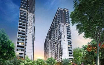 Deux immeubles modernes de grande hauteur, baptisés « Sobha Creek Vistas », se dressent sur un ciel crépusculaire, entourés d'une verdure luxuriante et un couple se promène dans le cadre serein du parc.
