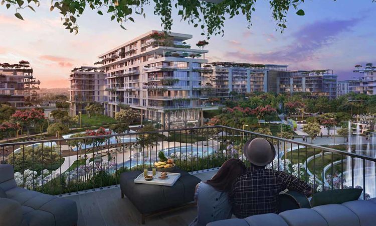 A couple sits on a sofa enjoying a view of a luxurious residential complex with lush gardens and pools during a sunset near Central Park City Walk.