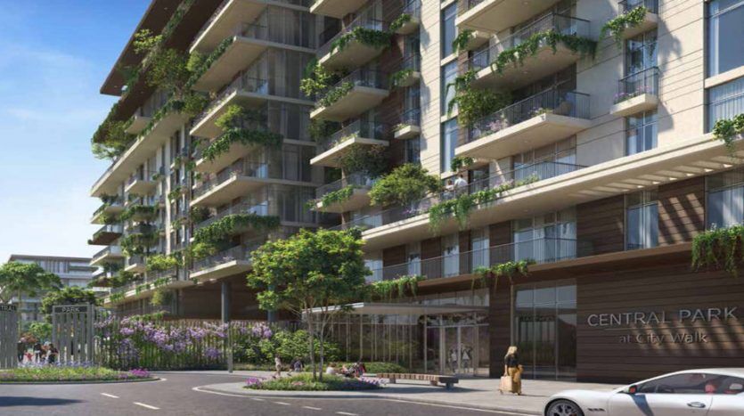 A modern apartment building with extensive greenery on the balconies, a spacious tree-lined driveway and parked cars under clear skies. The sign reads "Central Park City Walk".