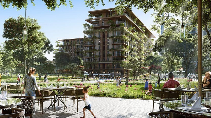 A lively outdoor restaurant scene with people dining at tables adorned with white tablecloths in Central Park. In the background, modern apartments surrounded by lush landscaped gardens and towering trees. A child runs