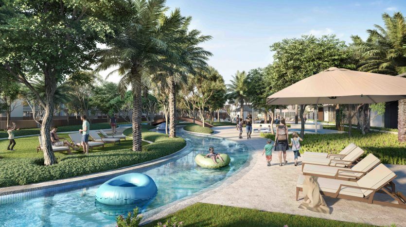 Une scène de villégiature animée dans Arabian Ranches 3 avec des gens profitant d'une journée ensoleillée au bord d'une piscine sinueuse entourée d'une verdure luxuriante et de palmiers. Certains se prélassent sur des transats pendant que d'autres marchent