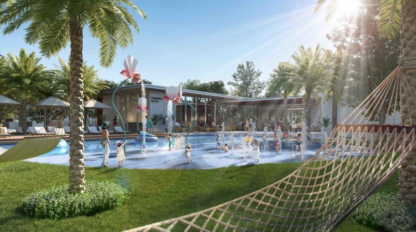 Une scène ensoleillée d'Arabian Ranches 3 avec des palmiers, une piscine, une pataugeoire avec jets d'eau où les enfants jouent et un hamac au premier plan, représentant un environnement détendu et amusant.