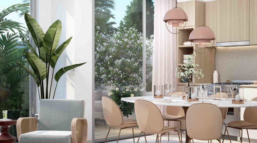 Une salle à manger élégante dans Arabian Ranches 3 comprenant une table moderne avec des chaises beiges, un fauteuil confortable, de grandes fenêtres avec vue sur le jardin, des suspensions roses et une plante d'intérieur luxuriante.