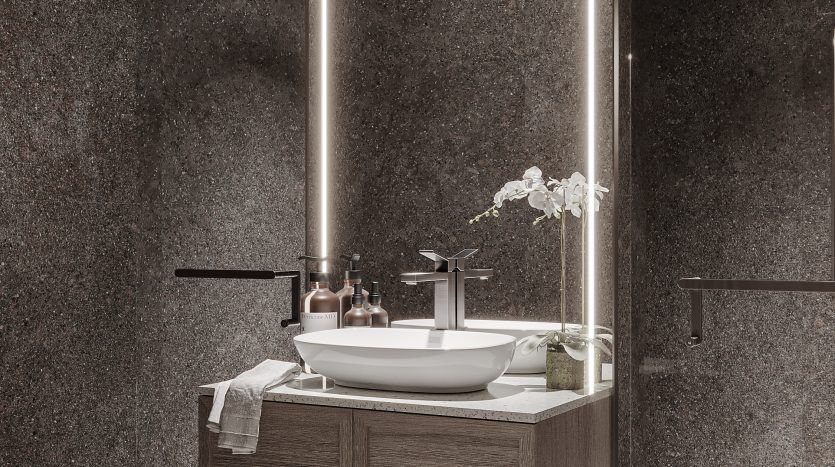 Salle de bain moderne dotée d'une élégante vanité en bois avec un lavabo ovale, entourée d'un grand miroir Oxford 212, adossé à un mur texturé gris chiné. Les serviettes roulées et les articles de toilette sont soigneusement disposés