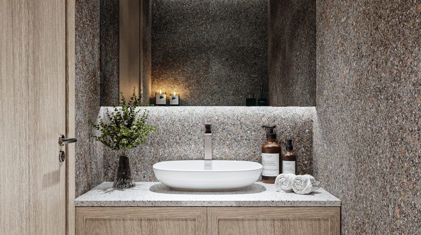 Salle de bains moderne dotée d'une vanité en bois avec un lavabo blanc Oxford 212, des murs en granit et des serviettes blanches soigneusement empilées. Des bougies décoratives et des articles de toilette sont disposés sur le comptoir.
