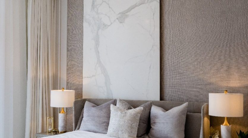 Chambre moderne comprenant un grand lit avec des draps texturés, flanqué de lampes de table sur les tables de nuit, sous un lustre sphérique unique, sur fond d'Oxford 212 et de panneaux muraux texturés.