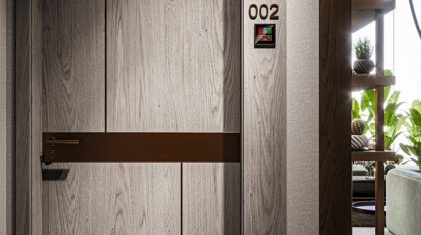 Une porte d'ascenseur moderne avec une finition en bois, une poignée en laiton et le numéro de chambre 212 affiché à côté d'un indicateur d'étage lumineux dans un cadre intérieur élégant.