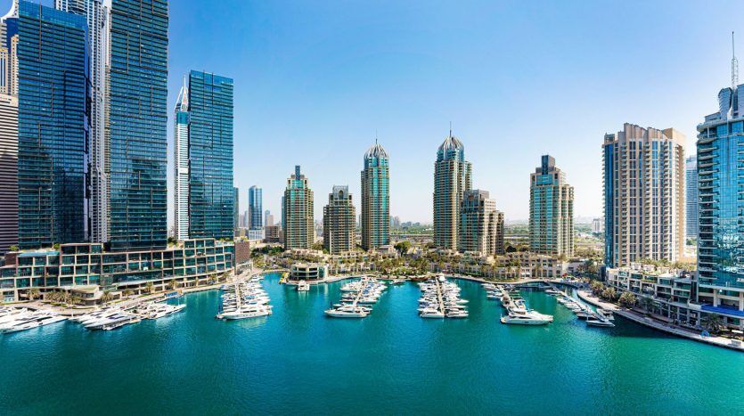 Une vue panoramique sur une marina animée entourée d'immeubles modernes de grande hauteur sous un ciel bleu clair. L'eau est parsemée de nombreux bateaux et yachts, présentant un emplacement idéal pour investir dans le quartier de Dubaï.