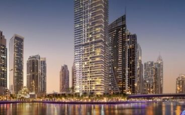 Gratte-ciels le long d'un front de mer à Dubaï illuminés au crépuscule, avec des reflets dans l'eau et une passerelle qui les traverse.