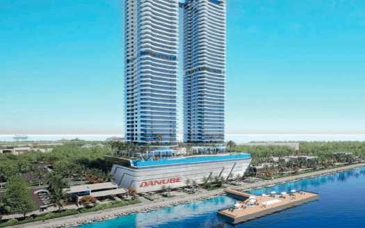 Vue aérienne d'un gratte-ciel moderne au bord de l'eau à Dubaï, affichant le logo « Danube » à sa base. Des arbres et une marina avec des bateaux sont visibles le long du rivage.