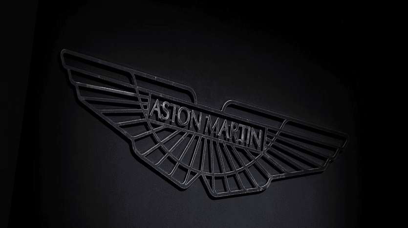Close-up image of an elegant black Aston Martin logo depicted with stylized wings and the brand name embossed in the center on a dark background.