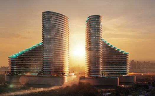 Deux gratte-ciel modernes et incurvés avec des balcons illuminés se tiennent côte à côte au coucher du soleil, avec le soleil brillant entre eux et la ligne d'horizon de la ville visible à l'arrière-plan.