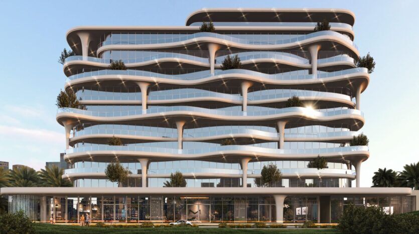 Coralis, un bâtiment moderne de plusieurs étages, présente des balcons courbes et ondulés, des murs de verre et des arbres à différents niveaux, sur fond de ciel clair et de verdure au premier plan.