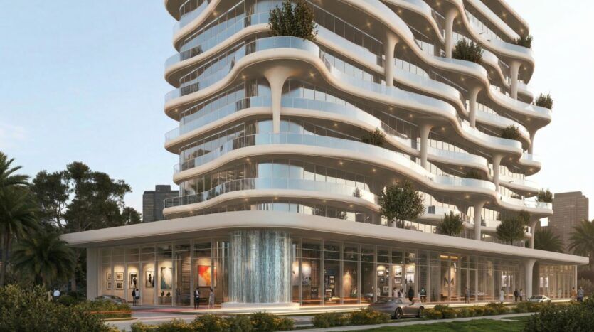 Bâtiment moderne de type Coralis avec des balcons blancs incurvés et de grandes baies vitrées, avec des terrasses verdoyantes et une galerie d'art ou un café au rez-de-chaussée avec des personnes à l'intérieur. Des voitures et des arbres sont visibles devant.
