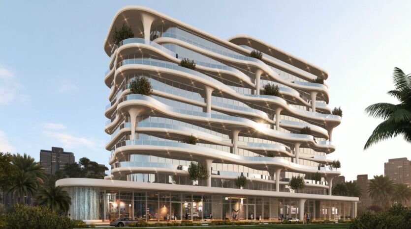 Immeuble Coralis moderne de plusieurs étages avec des balcons blancs incurvés, de grandes baies vitrées et des terrasses verdoyantes. Des palmiers et des voitures sont visibles au premier plan, avec un paysage urbain en arrière-plan.