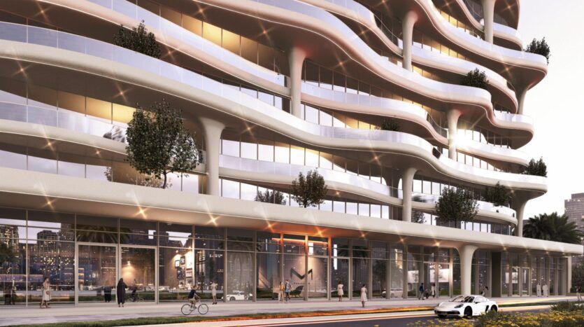 Un immeuble moderne de Coralis avec des balcons ondulés et incurvés, de grandes baies vitrées et de petits arbres sur les balcons. Des gens marchent et font du vélo sur le trottoir en contrebas, tandis qu'une voiture de sport blanche est garée dans la rue devant l'immeuble.