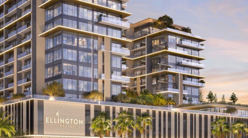 Immeuble moderne de plusieurs étages, doté de grandes baies vitrées et de balcons, baigné d'une lumière jaune. Des palmiers et des plantes ornent l'entrée, tandis que l'enseigne « Everly Place by Ellington » est visible sur la façade.