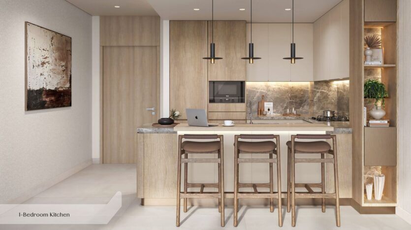 Cuisine moderne à Everly Place, signée Ellington, avec des meubles en bois clair, un dosseret en pierre et un îlot équipé de trois tabourets de bar marron. Des suspensions éclairent l'espace, tandis que des œuvres d'art et des plantes apportent une touche chaleureuse ; un ordinateur portable est posé sur le plan de travail.