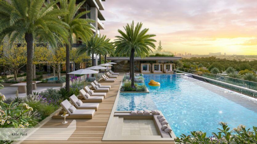 L'espace piscine extérieur luxueux de l'Everly Place by Ellington offre, au coucher du soleil, des chaises longues, des parasols, des palmiers et un aménagement paysager luxuriant. Une pataugeoire pour enfants se trouve au premier plan, tandis qu'une bouée jaune flotte dans le bassin principal. La silhouette de la ville se profile au loin.