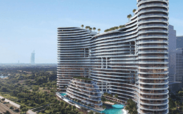 Un gratte-ciel moderne et incurvé, Binghatti Aquarise, avec des façades en verre et des toits verts, se dresse à côté d'une piscine, entouré d'un paysage luxuriant, avec une tour emblématique lointaine visible contre le ciel bleu.