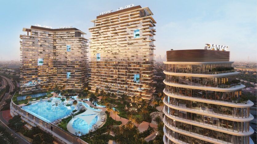 Un complexe moderne d'immeubles de grande hauteur avec des balcons uniques en quinconce, doté d'une grande piscine centrale au milieu des palmiers. Situés dans le quartier Damac de Dubaï, les bâtiments arborent le logo "DAMAC" et surplombent un paysage urbain au coucher du soleil.