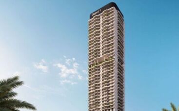 Un grand immeuble moderne avec de nombreux balcons se dresse dans un ciel bleu clair. Le nom "Alta View" figure au sommet de l'immeuble. Des feuilles de palmier sont visibles dans le coin inférieur gauche.
