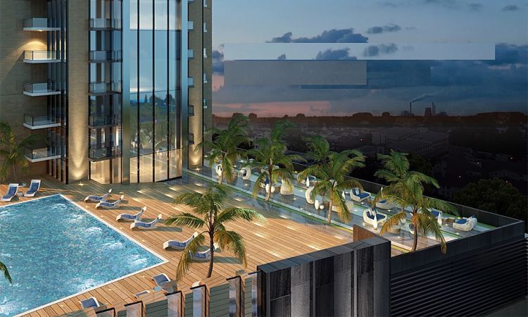 Un luxueux espace piscine sur le toit au crépuscule, comprenant une piscine illuminée en bleu, des chaises longues et des palmiers, avec la tour carrée visible en arrière-plan du paysage urbain.