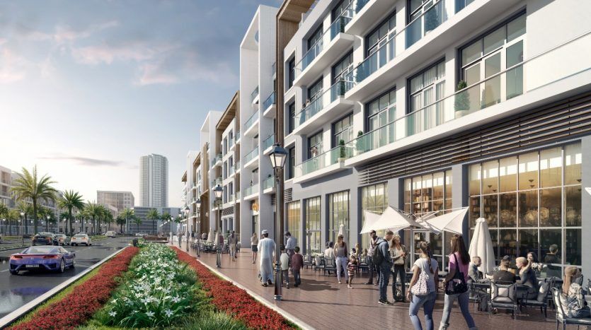 Scène de rue urbaine moderne avec des piétons passant devant des cafés en plein air, une séparation centrale paysagée et des bâtiments contemporains, dont le Panthéon Elysée, sous un ciel clair.
